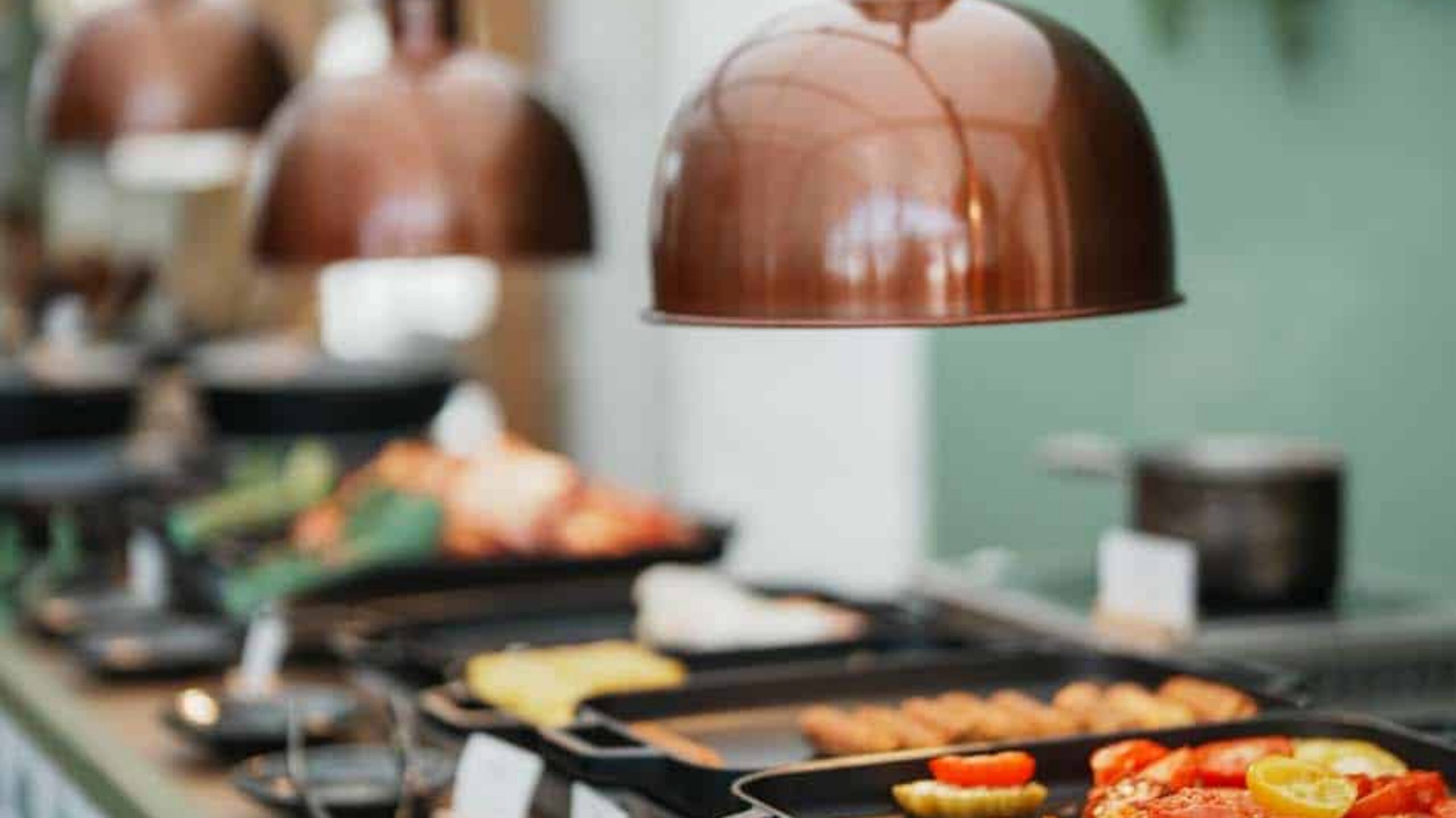 Plated dishes under copper cloches on the kitchen pass
