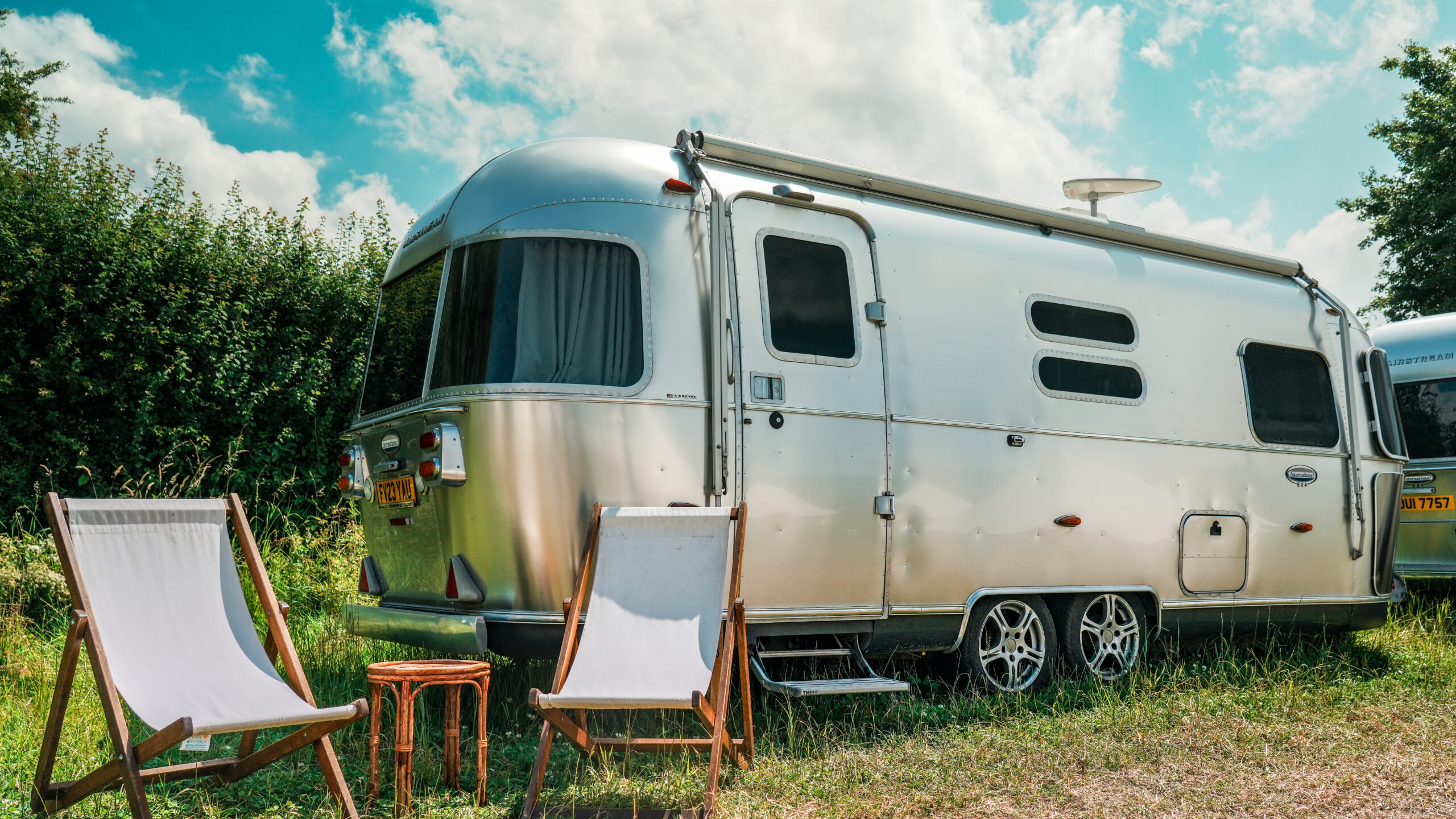 A silver Airstream caravan with deckchairs set out on the grass